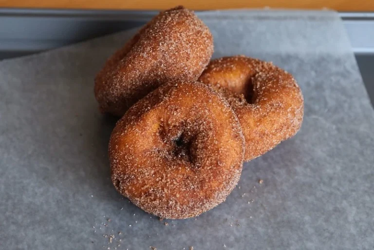 A freshly baked cake donut with a golden-brown crust, topped with a light glaze and sprinkles, resting on a wooden board.