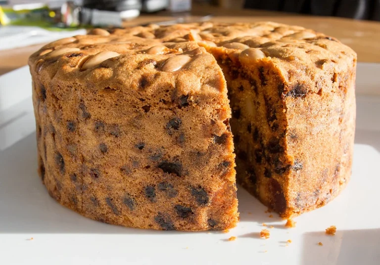 A beautifully baked fruit cake topped with glazed fruits and nuts, served on a wooden platter.