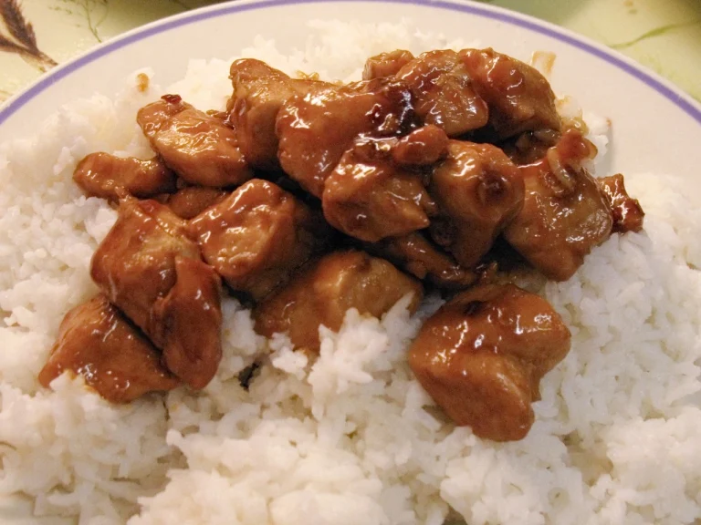 A plate of bourbon chicken served with a side of rice and vegetables, glazed with a shiny, caramelized bourbon sauce.