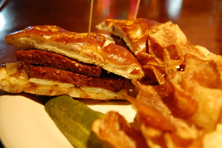 A close-up of sliced bologna on a wooden cutting board, garnished with fresh parsley and served alongside mustard and crackers.