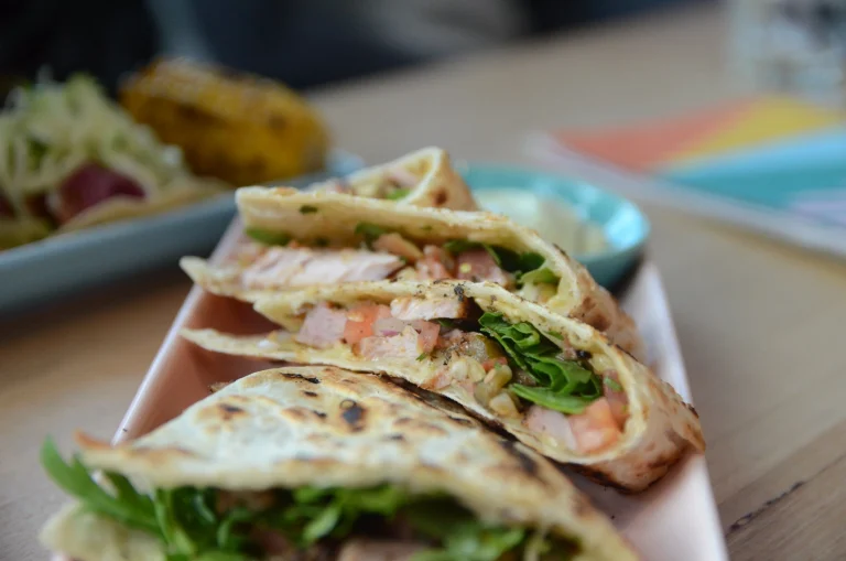 A freshly prepared quesadilla, golden and crisp, filled with melted cheese and savory ingredients, served on a wooden plate with a side of salsa and guacamole.