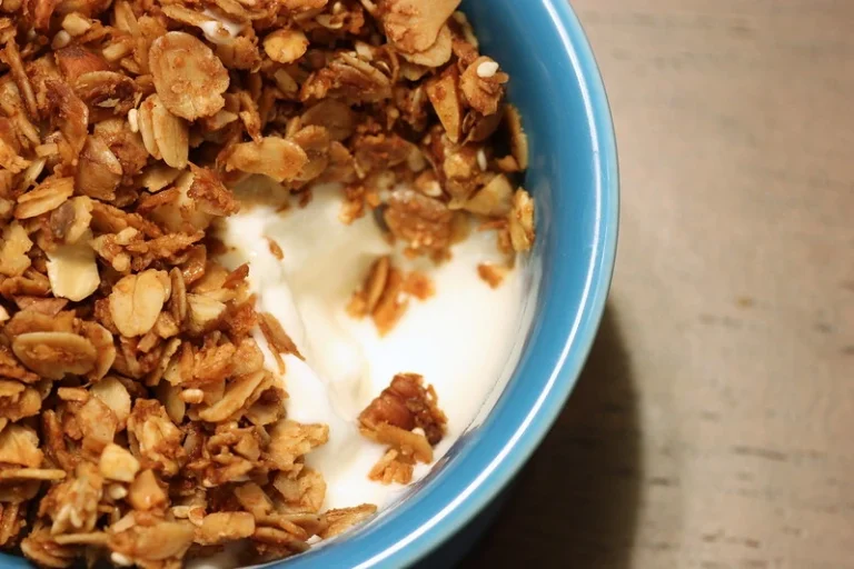 A colorful bowl of breakfast cereal with milk, topped with fresh fruit, on a wooden table.