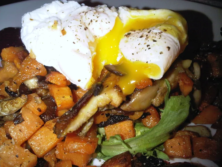 A hearty sweet potato breakfast hash with diced sweet potatoes, bell peppers, onions, and sunny-side-up eggs in a cast-iron skillet.