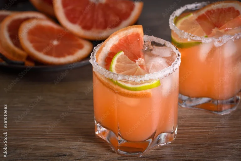 A refreshing Paloma cocktail served in a tall glass, garnished with a slice of grapefruit and a sprig of fresh rosemary, with a salt-rimmed edge.