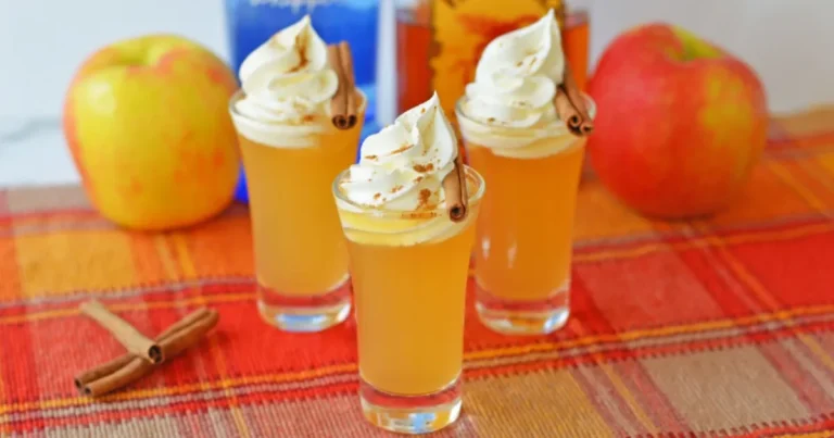 Close-up of cinnamon sugar-rimmed Apple Pie Shots garnished with cinnamon sticks on a rustic wooden table.