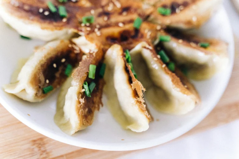 A plate of freshly steamed dumplings with a side of dipping sauce.