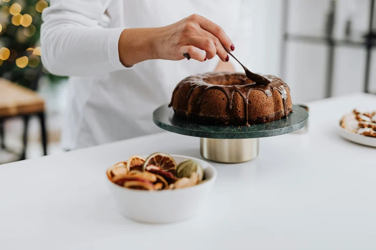 A moist and golden pumpkin bundt cake topped with a creamy glaze, garnished with a sprinkle of cinnamon, sitting on a rustic wooden table.