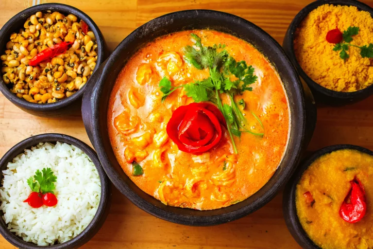 A vibrant bowl of red curry with tender vegetables and chicken, topped with fresh basil leaves, served alongside a bowl of steamed rice.