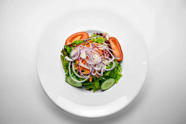 A colorful bowl of fresh cabbage salad with shredded green and red cabbage, carrots, and a light dressing, garnished with fresh herbs.