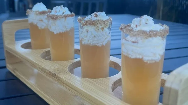 Close-up of Apple Pie Shots served in cinnamon sugar-rimmed shot glasses with a cinnamon stick garnish