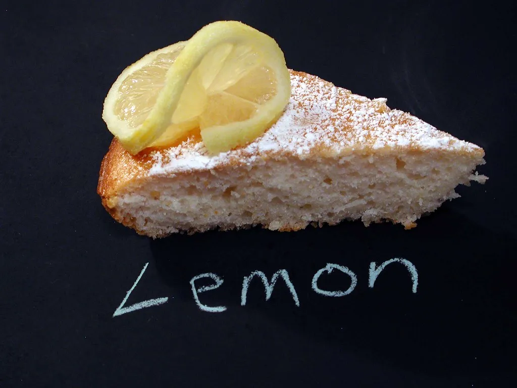 A slice of angel food cake with creamy lemon pie filling on a white plate, garnished with fresh lemon zest