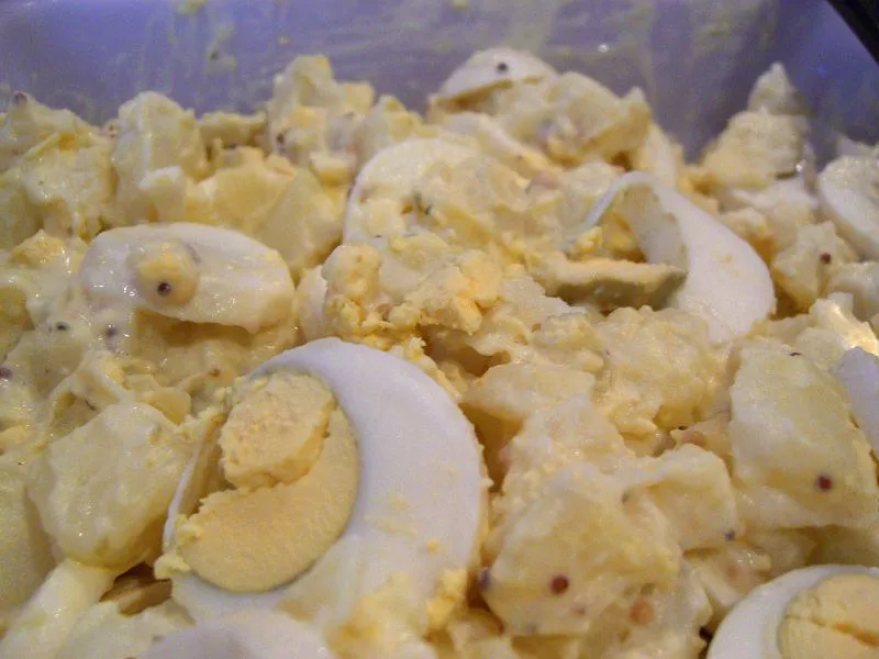 A creamy homemade potato and egg salad served in a white bowl, garnished with fresh parsley and a sprinkle of paprika.