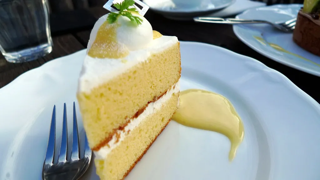 A slice of angel food cake with creamy lemon pie filling on a white plate, garnished with fresh lemon zest
