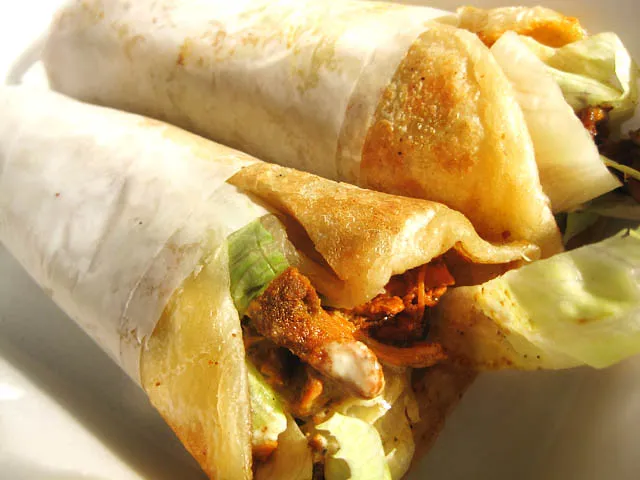 A freshly made Kathi Roll filled with spiced grilled chicken, sautéed onions, and tangy chutneys, wrapped in a soft, flaky paratha and served on a wooden plate.