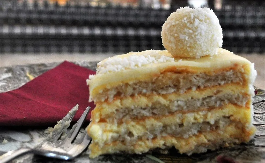 A slice of homemade coconut cake with creamy frosting and toasted coconut, placed on a white ceramic plate