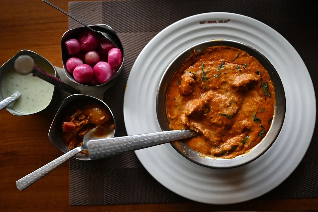 A bowl of creamy Butter Chicken with tender, marinated chicken pieces simmered in a rich, spiced tomato and butter sauce, garnished with fresh cilantro and served with naan and basmati rice.