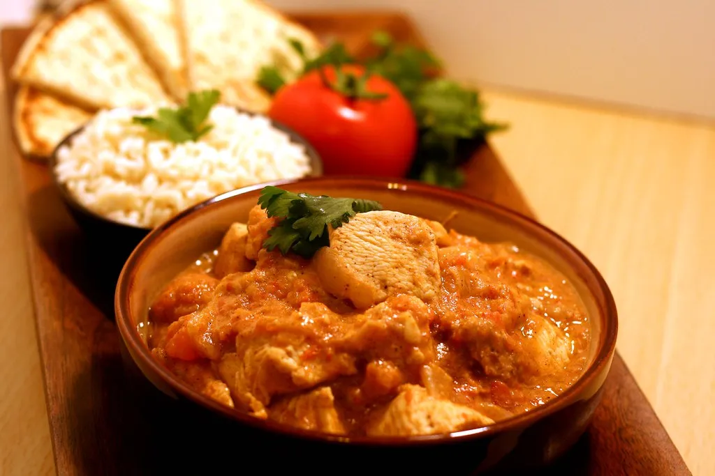 A bowl of creamy Butter Chicken with tender, marinated chicken pieces simmered in a rich, spiced tomato and butter sauce, garnished with fresh cilantro and served with naan and basmati rice.