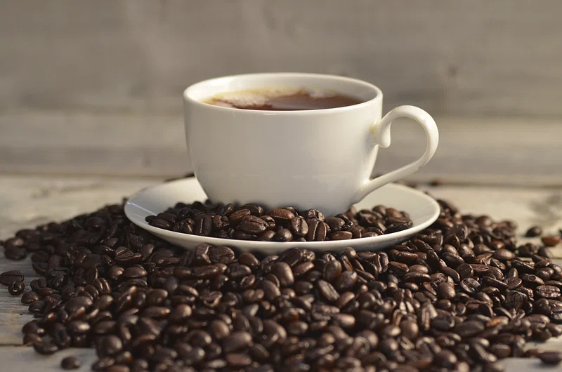 A close-up of high-quality coffee beans, dark and glossy, spilling from a burlap sack onto a wooden surface.