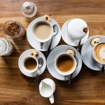 A steaming cup of freshly brewed coffee in a ceramic mug, placed on a cozy wooden table with scattered coffee beans and a soft morning light in the background.