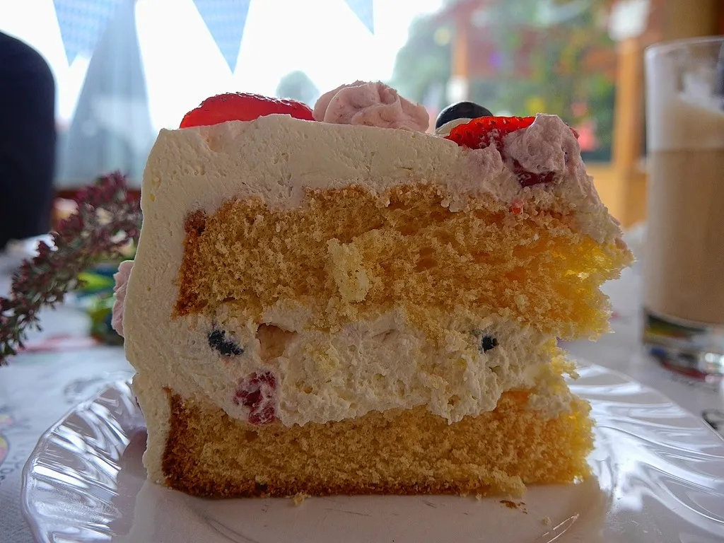 A slice of fluffy white cake with layers of strawberries and whipped cream on a dessert plate.