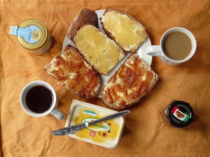 A steaming cup of classic black coffee next to a slice of whole-grain toast topped with creamy nut butter and banana slices, served on a wooden plate.