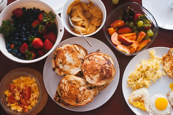 A healthy breakfast plate with a poached egg on whole-grain toast, avocado slices, a side of sautéed spinach, and fresh fruit including strawberries and blueberries, served with a glass of orange juice.