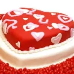 A freshly baked heart-shaped cake decorated with red frosting and sprinkles.