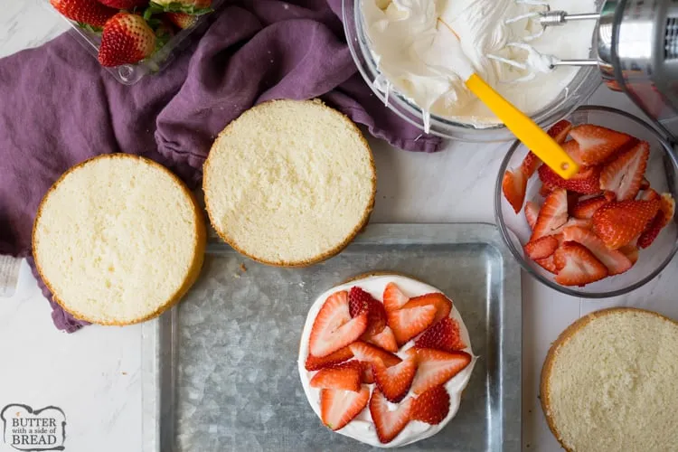 Fresh strawberries, cake flour, butter, eggs, and sugar arranged on a kitchen countertop.