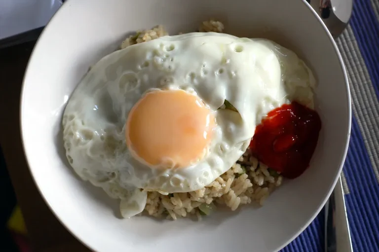 A delicious breakfast rice bowl topped with fresh berries, sliced banana, and a drizzle of honey, served in a white ceramic bowl on a wooden table.