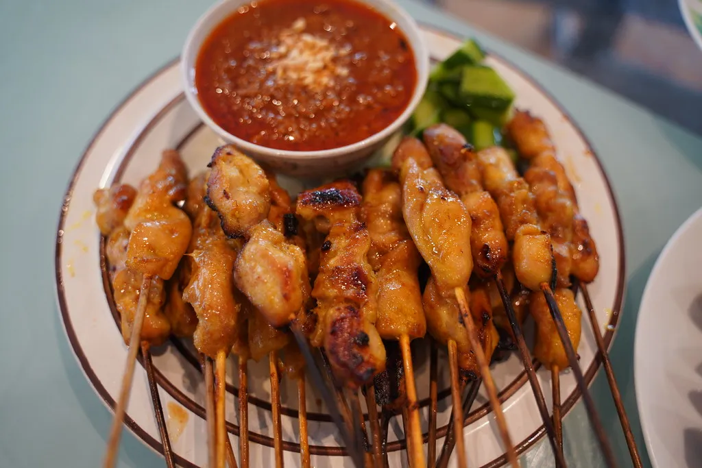 Skewered and grilled satay served with a creamy peanut sauce, accompanied by cucumber slices and rice cakes.