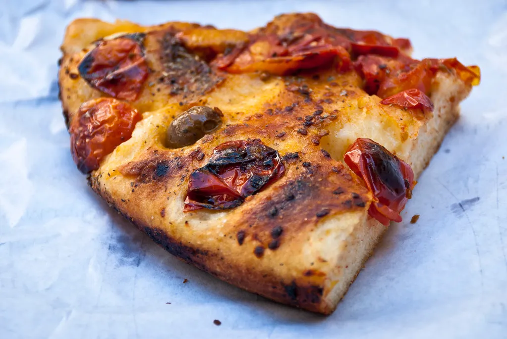 Freshly baked focaccia pizza topped with cheese, herbs, and a drizzle of olive oil, served on a wooden board