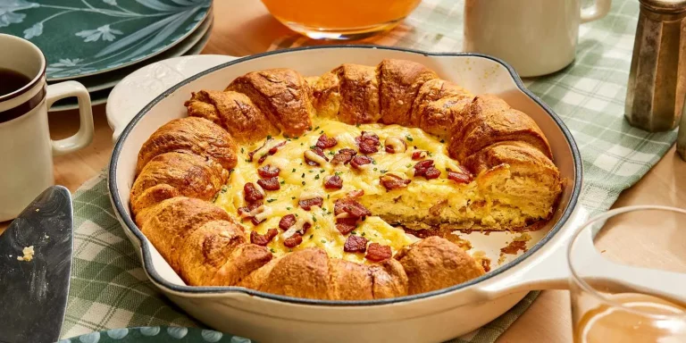 Golden, flaky croissant breakfast pie with a crispy crust, filled with creamy custard and fresh fruit, served on a white plate