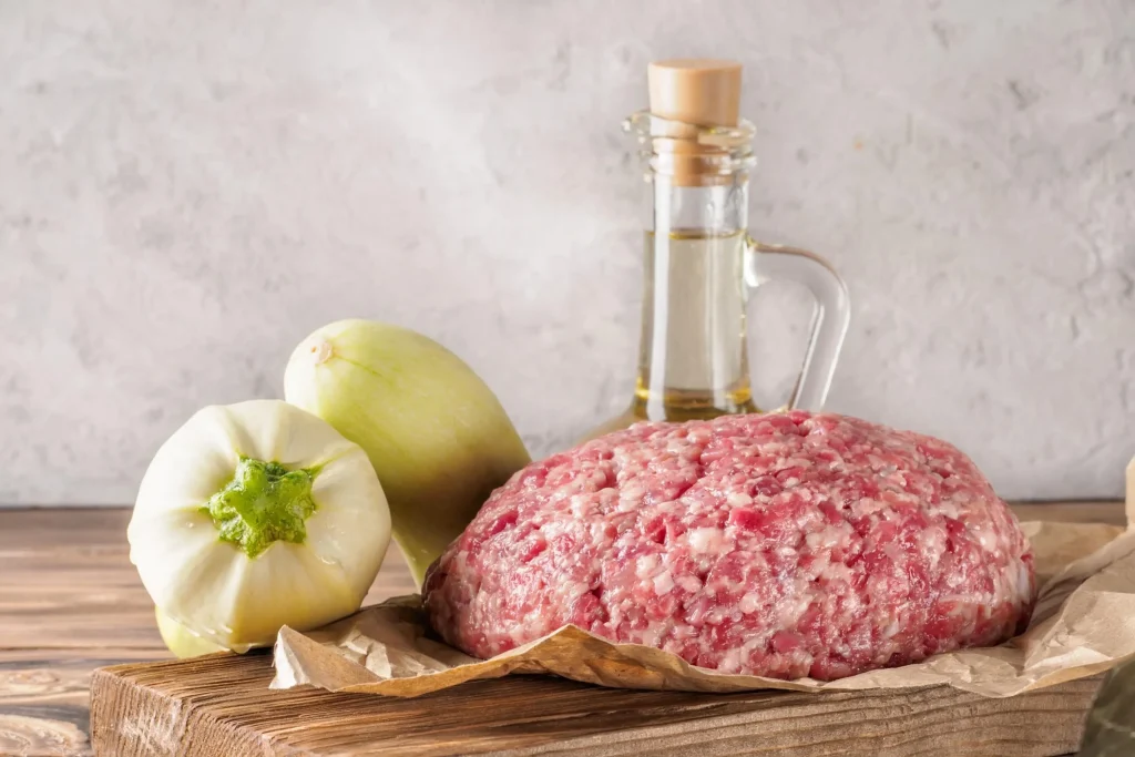 Fresh meat being ground using a meat grinder for homemade peppercorn sausages.