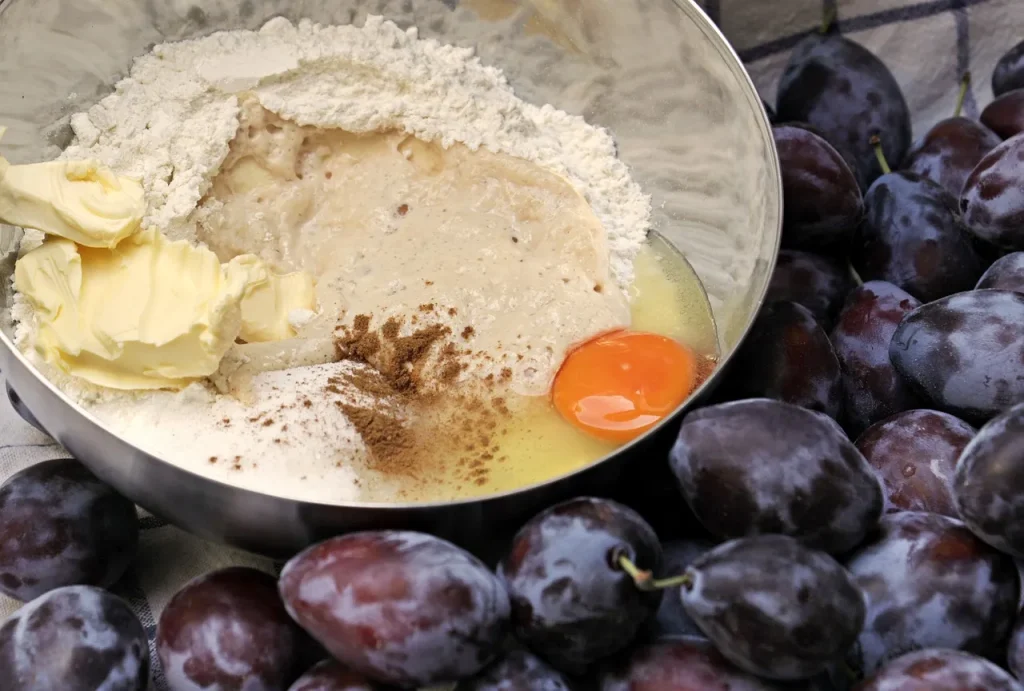 Mixing cake batter in a bowl with flour, sugar, butter, eggs, and cherry blossom flavoring, using a spatula and hand mixer.