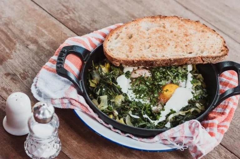 A bowl of creamy and cheesy spinach garnished with grated Parmesan and freshly ground black pepper, served in a white dish.