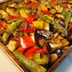 Rustic Italian roasted vegetables on a baking sheet, including zucchini, bell peppers, cherry tomatoes, and red onion, garnished with fresh herbs.