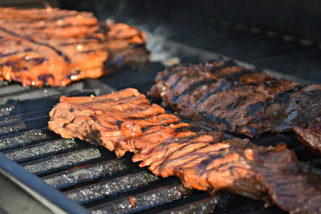 Juicy grilled skirt steak with perfect char marks, served on a wooden board with fresh herbs and a side of dipping sauce.