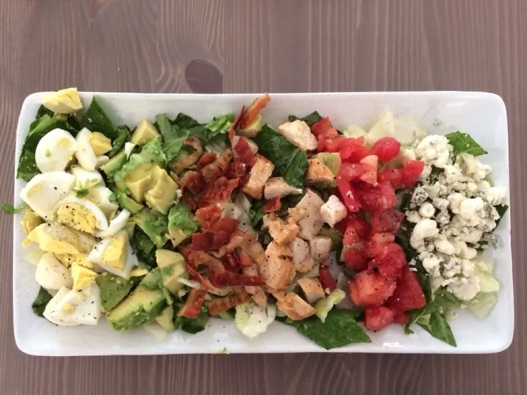 Fresh and colorful Cobb salad with grilled chicken, crispy bacon, avocado, hard-boiled eggs, and blue cheese crumbles on a bed of romaine lettuce