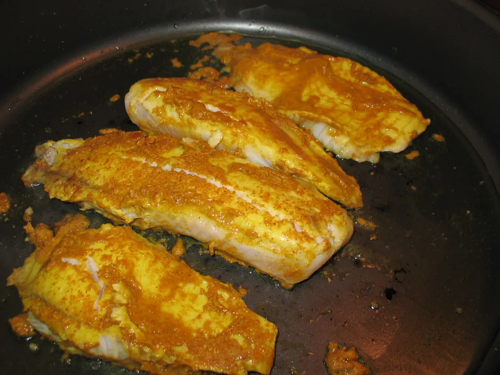 Golden-brown baked fish fillets garnished with fresh herbs and lemon slices on a white plate