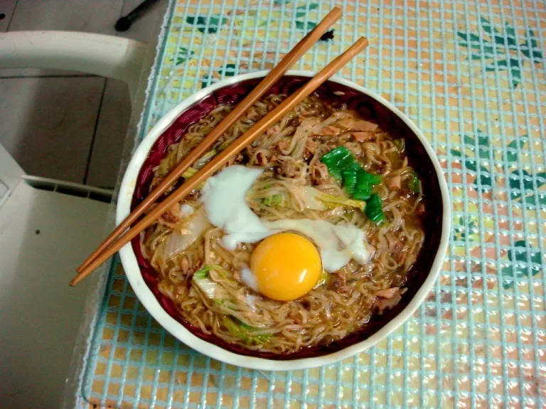 A bowl of creamy chicken and egg noodles garnished with fresh herbs, served on a rustic wooden table.