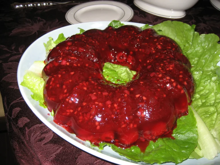 Vibrant cranberry Jello salad topped with whipped cream and garnished with cranberries in a glass serving bowl