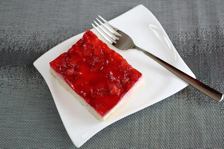 Slice of cranberry gelatin salad on a white plate with creamy topping"