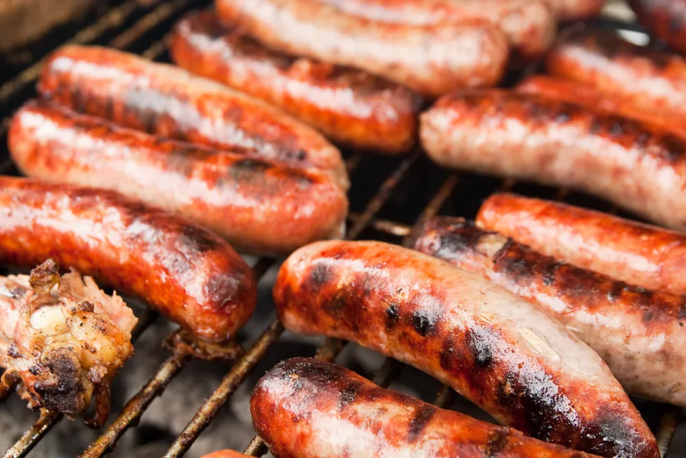 Freshly made beef Italian sausage links resting on a wooden cutting board with herbs and spices