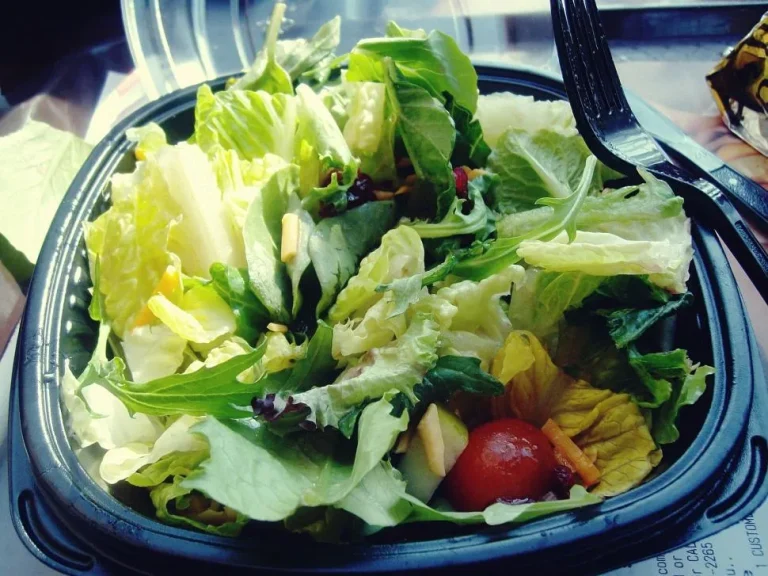 A fresh green salad with crisp lettuce, cherry tomatoes, cucumbers, and a drizzle of dressing in a bowl.