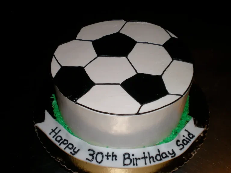A delicious and creatively decorated soccer cake shaped like a soccer ball, complete with grass icing and a goalpost, perfect for soccer-themed parties.