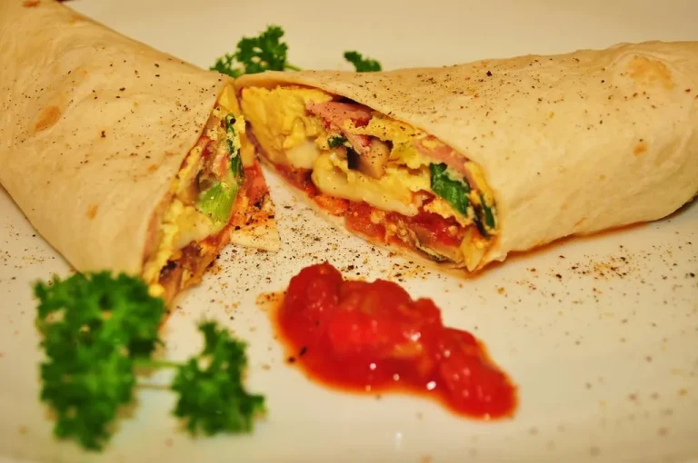 Delicious and crispy breakfast burrito filled with scrambled eggs, bacon, and cheese, served with fresh avocado on the side.
