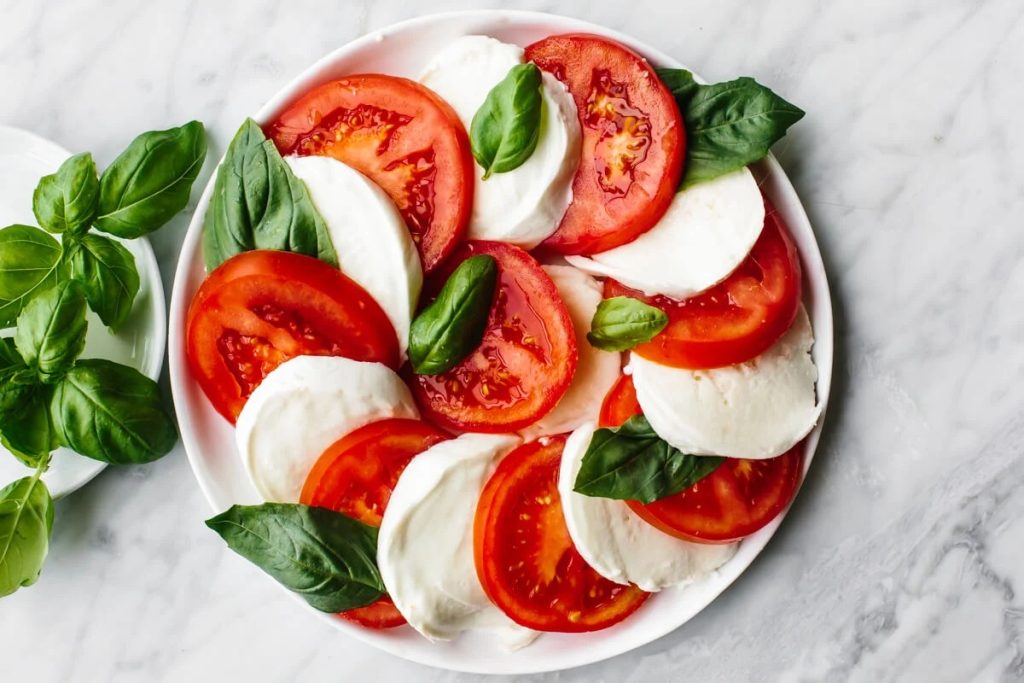 Fresh tomato mozzarella salad drizzled with extra virgin olive oil and balsamic glaze, garnished with basil leaves and a sprinkle of sea salt