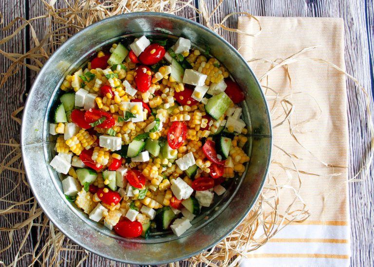 Bowl of creamy Elote Pasta Salad with roasted corn, cotija cheese, and fresh cilantro, topped with chili powder and lime wedges.