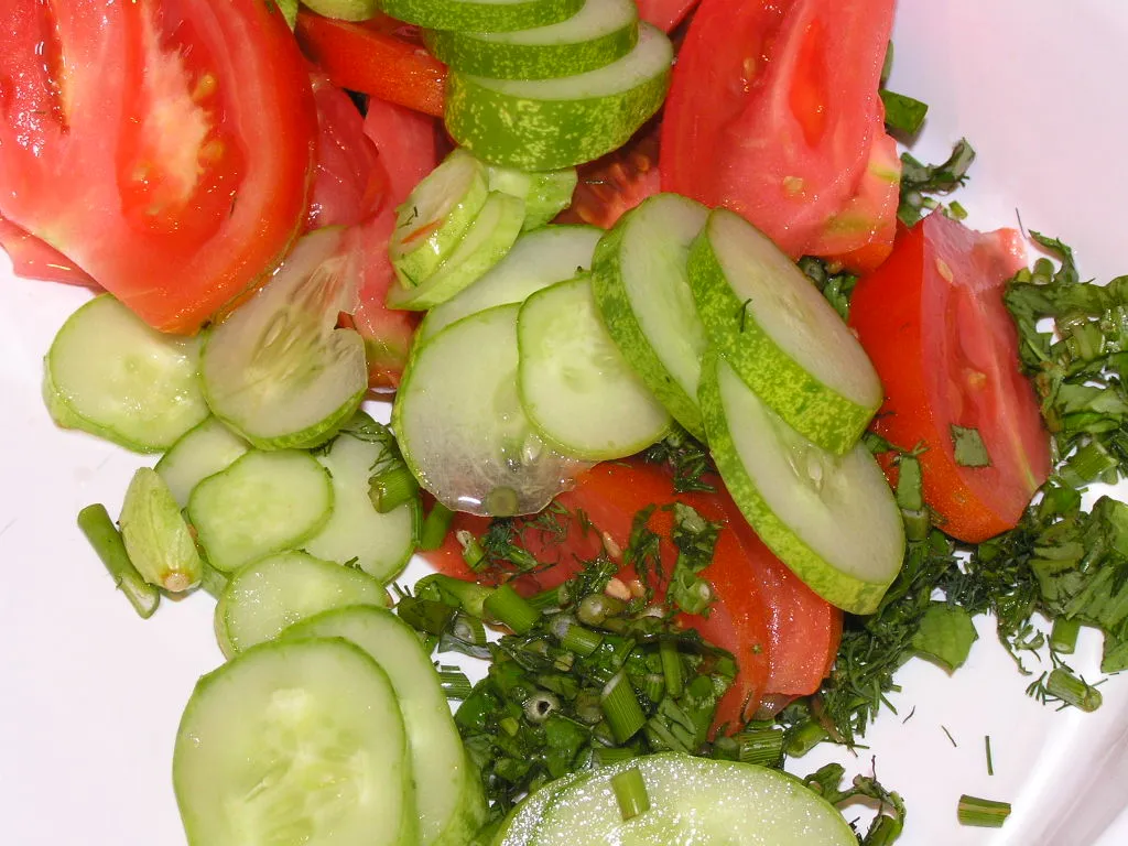 Chopping fresh tomatoes and cucumbers on a wooden cutting board