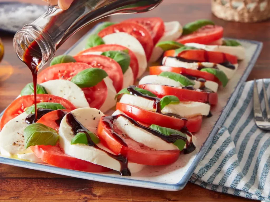 Evenly sliced ripe tomatoes and fresh mozzarella cheese arranged in alternating layers on a white plate